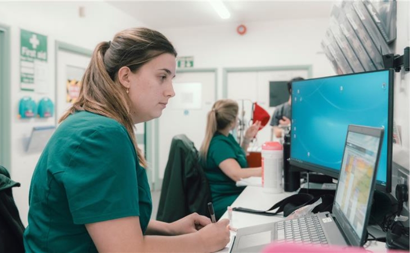 Veterinary professional sat in green uniform at her desk, working on the computer