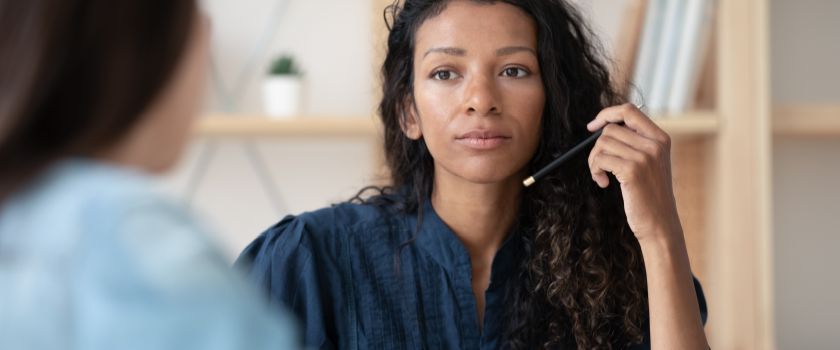 A young Black woman with a focused demeanour engages in conversation with a co-worker in a professional office setting.