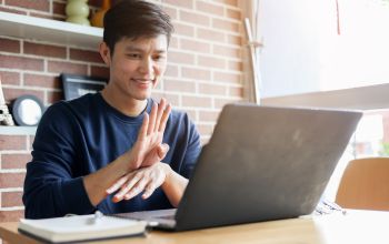 An East Asian man utilises sign language to interact through a laptop.