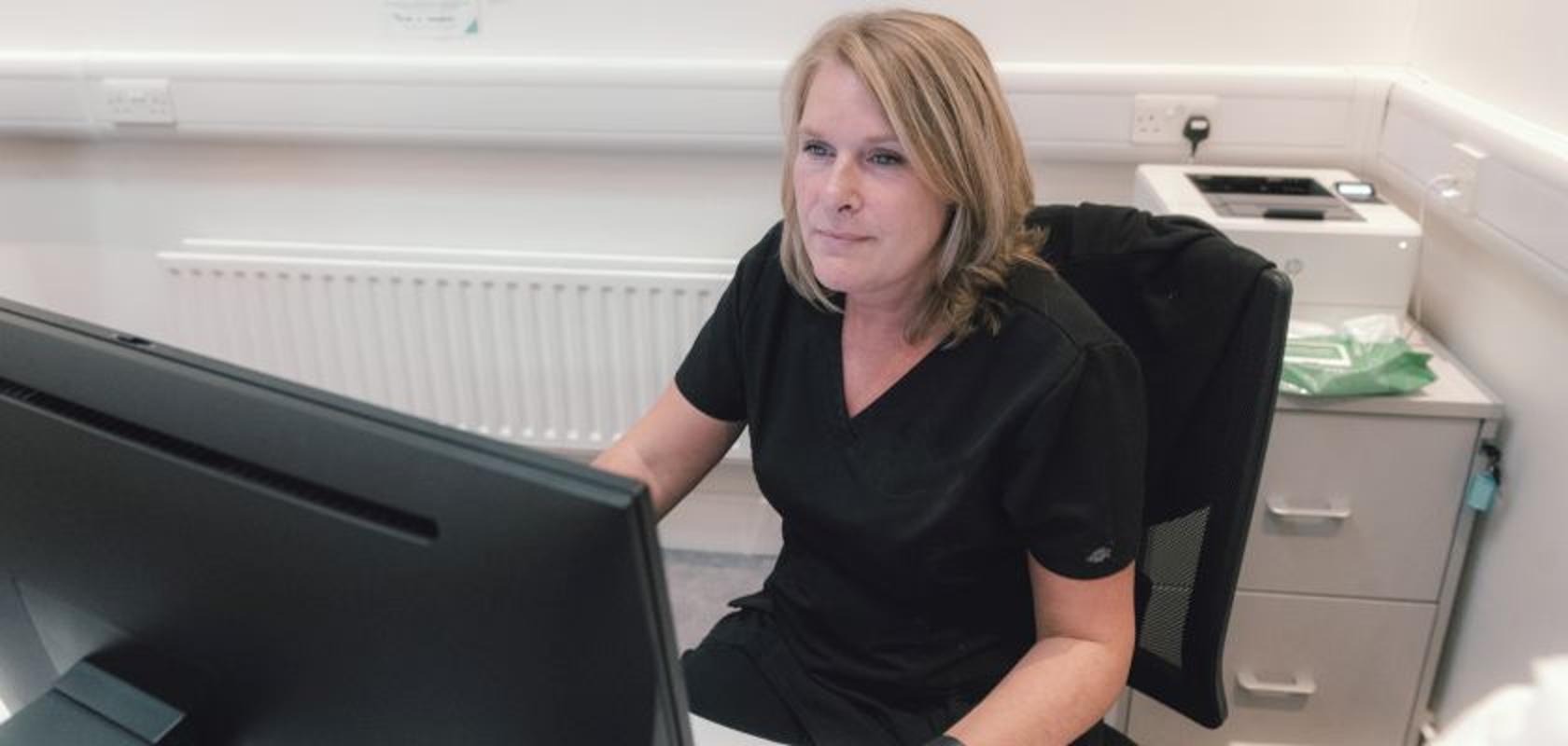 A female veterinary practice staff member sitting at a desk and looking at a computer monitor.