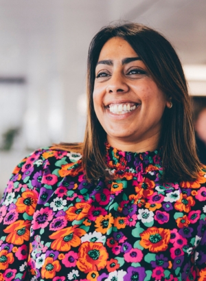 A photo of Rapinder Newton, a woman with brown hair wearing a colourful top, smiling