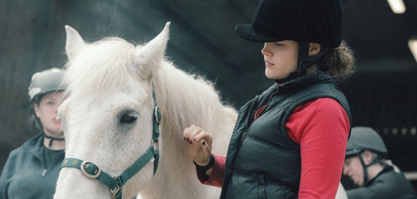 A female veterinary student standing beside a grey horse