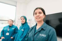 Three Surrey Vet School students wearing scrubs stand in a line looking at the camera